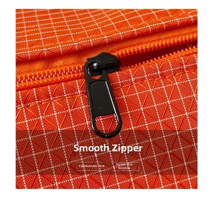 Détail macro d'une fermeture éclair en métal noir sur un sac en nylon orange à carreaux