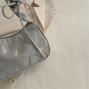 Silver-grey pleated underarm bag with metal bow detail on a beige blazer background