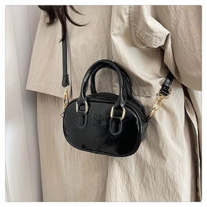 Close-up of black glossy leather mini bag with gold hardware and logo on beige trench coat