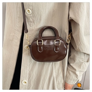 Detail of dark brown patent leather mini bag with embossed logo and golden hardware