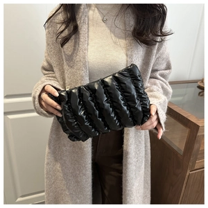 Detail of glossy black quilted pouch with gold zipper held by a model in beige coat