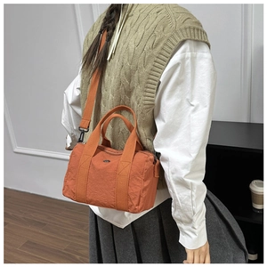 Action shot of orange nylon crossbody bag with adjustable strap on white shirt model