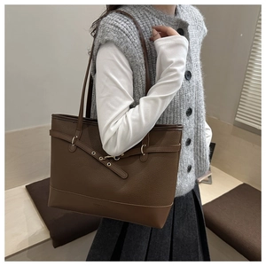 Brown leather tote bag featuring a decorative strap with gold eyelets and textured finish