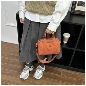 Detailed side view of orange nylon crossbody bag with multiple zippers and wide strap
