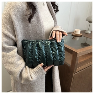 Detail einer dunkelgrünen gesteppten Clutch-Tasche mit Glanz-Finish von Model gehalten