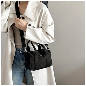 Detail of black nylon mini barrel bag showing detachable strap and metal logo on the front