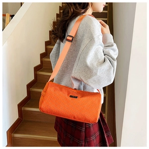 Détail d'un sac bandoulière orange à carreaux en nylon porté avec bandoulière réglable