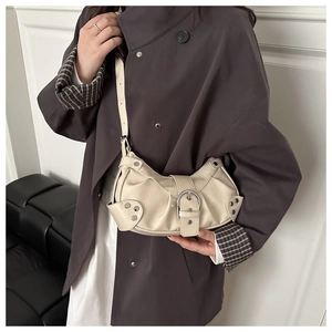 Detail of a creamy white pleated half-moon bag featuring silver buckles and studs on a model