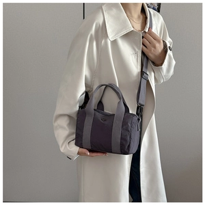 Detail of grey nylon crossbody bag shown on a model wearing an ivory trench coat