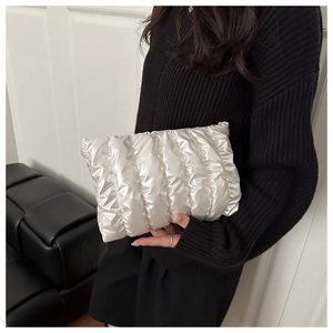 Detail of a pearl white pleated clutch bag with metallic texture held by a model