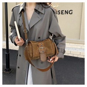 Détail du sac bandoulière en daim marron foncé avec grande boucle en métal et bandoulière
