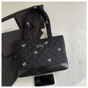 Detail of black quilted tote bag featuring white bow embroidery and metallic bow charm