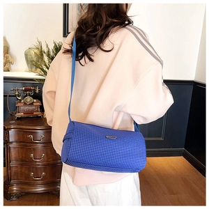 Vue détaillée d'un sac bandoulière cylindrique à carreaux bleus porté par un mannequin chic