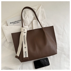 Detail of deep brown leather tote bag with stylish decorative ribbon on a soft background