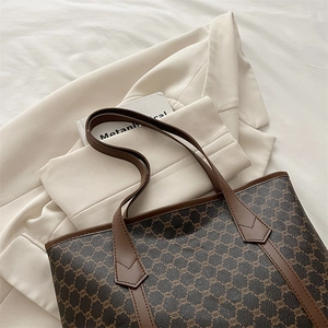 Classic brown monogram tote bag with leather straps on a cream suit, stylish large handbag