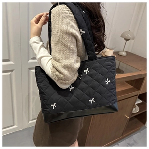 Detail view of black quilted tote bag with bow embroidery and reinforced leather bottom