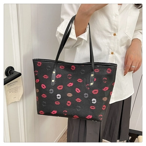 Close-up of the large black tote bag featuring colorful lip prints and gold rivet details