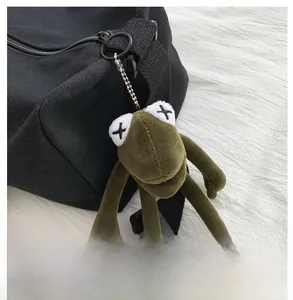 Dettaglio del portachiavi a forma di rana verde con occhi a X su borsa di tela