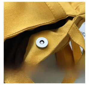 Gros plan du bouton magnétique argenté sur le sac en toile jaune avec doublure