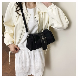 Détail du sac bandoulière noir avec œillets argentés et lanière en cuir sur modèle