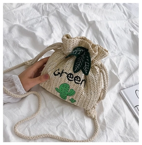 Top-down view of a beige straw bucket bag with green cactus embroidery and leaf details
