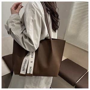 Detail of dark brown leather tote bag showing white decorative straps and fashion text