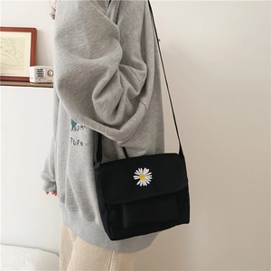 Detail of black canvas crossbody bag with white daisy embroidery and adjustable strap