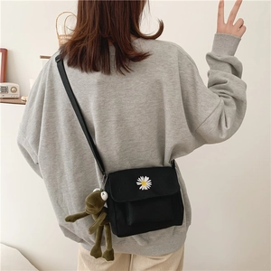 Close-up of black canvas crossbody bag with daisy print and green plush frog keychain