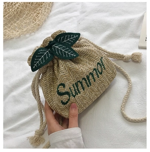 Detail of straw bucket bag with Summer embroidery and green leaf drawstring accents