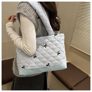 Detail of light blue quilted tote bag with embroidered black bows and metallic bow charm