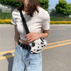 Detail of canvas cow print crossbody bag with cute plush cow charm and wide black strap