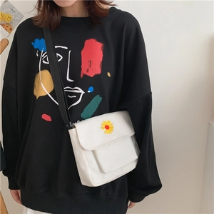 Detail view of a white canvas crossbody bag featuring yellow daisy embroidery and black strap