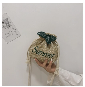 Detail of straw bucket bag featuring green leaf decor and Summer embroidery text