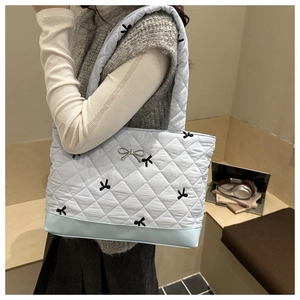 Detail of light blue quilted tote bag with black bow embroidery and wide shoulder strap