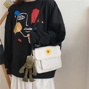 Detail of white canvas crossbody bag with daisy embroidery and green plush frog charm