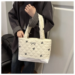 Close-up of quilted tote bag with black bow embroidery and silver metal bow charm details