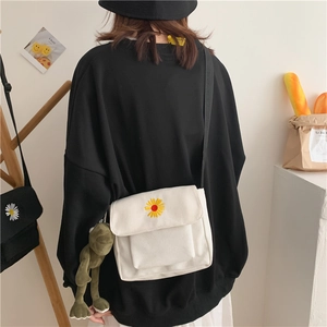 White canvas crossbody bag with daisy embroidery and a green frog plush toy charm