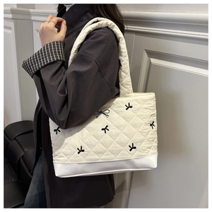 Quilted off-white tote bag with black bow embroidery and 3D ribbon charm on a model
