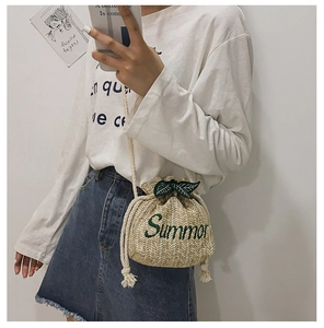Detail of beige straw bucket bag with green Summer embroidery and drawstring strap
