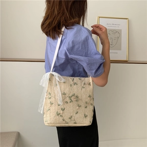Detail of straw woven shoulder bag with floral embroidery and lace bow on a model