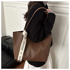 Dettaglio di grande borsa tote marrone con nastro decorativo indossata da una modella