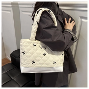 Close-up of quilted tote bag with black bow embroidery and metallic bow pendant detail