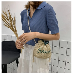 Detail view of woven straw bucket bag with green Summer embroidery on white skirt