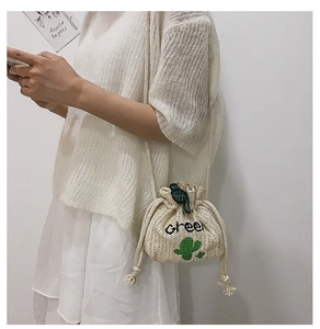 Detail of straw woven bucket bag featuring cactus embroidery and rope shoulder strap