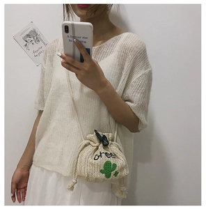 Detail of straw bucket bag featuring green cactus embroidery and drawstring closure