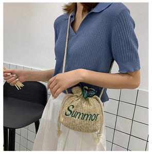 Detail of straw bucket bag with green leaf drawstrings and Summor embroidery