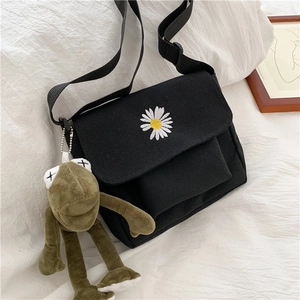 Detailed view of black canvas crossbody bag with white daisy embroidery and frog pendant
