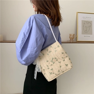 Detail of beige straw bag featuring green floral embroidery and a white lace bow accent