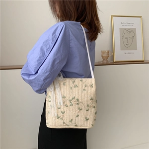 Detail of straw woven bucket bag with green leaf embroidery and lace bow accent