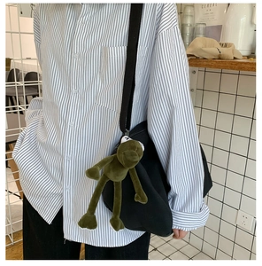 Grande borsa nera in tela con ciondolo a forma di rana verde sulla tracolla larga